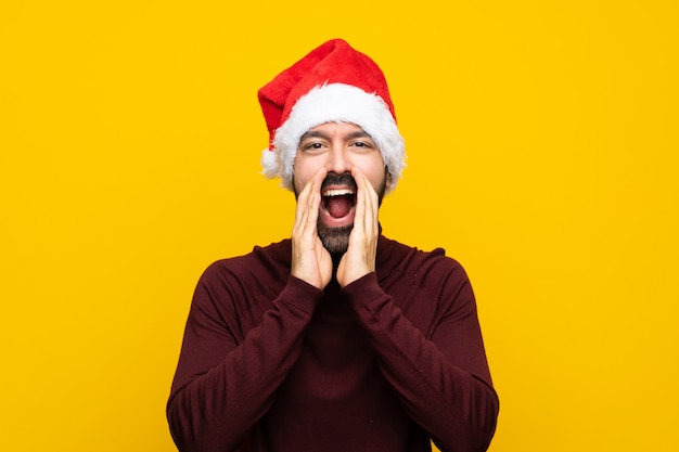 Homem com chapéu de natal isolado muro amarelo gritando e anunciando algo