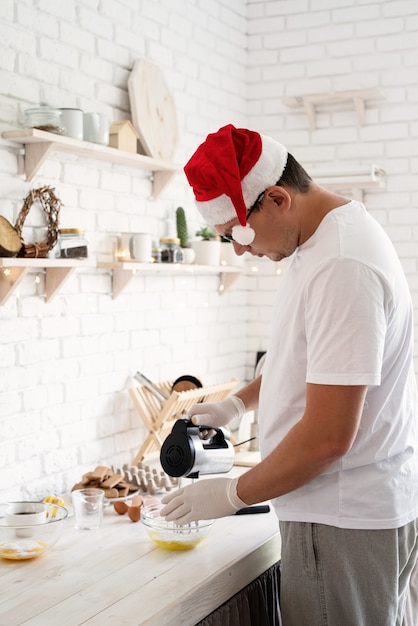 Homem com chapéu de papai noel fazendo merengue na mesa de madeira branca