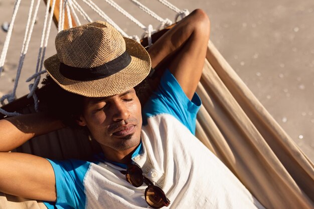 Foto homem com chapéu dormindo em uma hamaca na praia