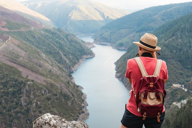 Homem com chapéu e mochila tirando foto da paisagem montanhosa com rio Copiar espaço Paicega Pesoz