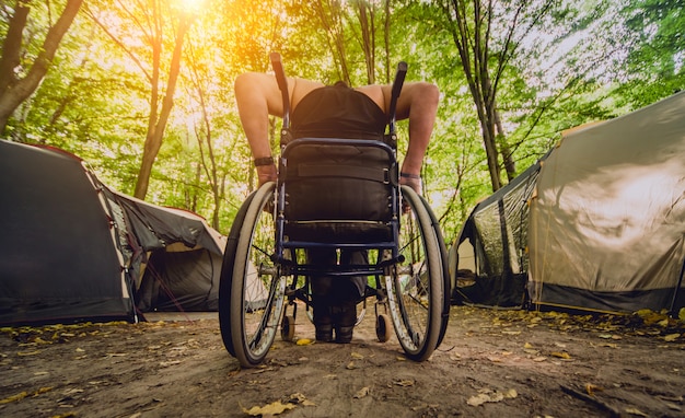 Homem com deficiência descansando em um parque de campismo com os amigos. cadeira de rodas na floresta
