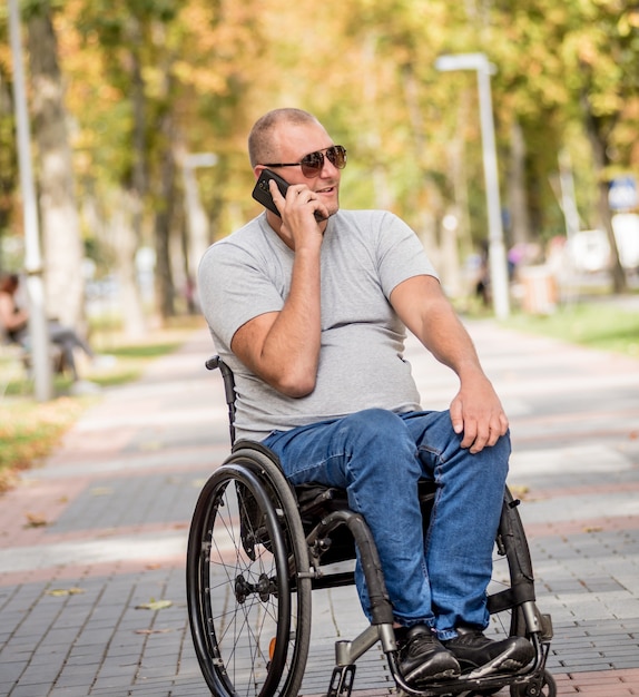 Homem com deficiência em cadeira de rodas no beco do parque usa um smartphone