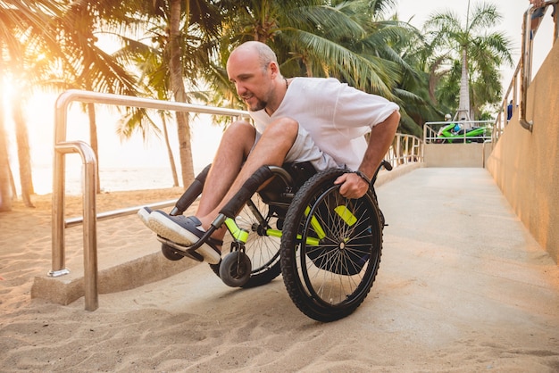 Homem com deficiência em cadeira de rodas se move em uma rampa para a praia.