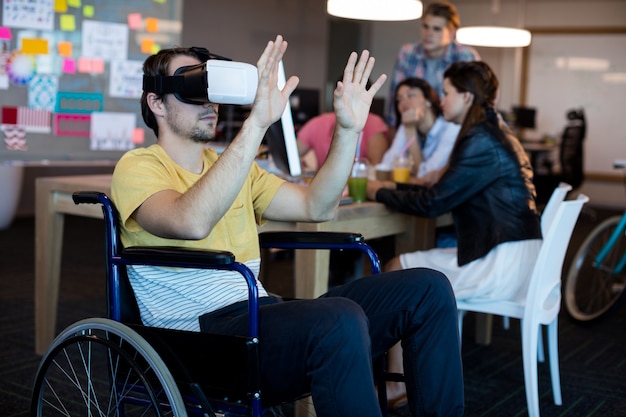 Homem com deficiência física em cadeira de rodas usando fone de ouvido VR no escritório