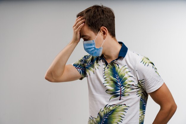 Homem com dor de cabeça com máscara médica azul isolada no fundo branco