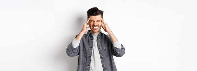 Homem com dor de cabeça fazendo careta e cerrando os dentes de enxaqueca dolorosa tocando cabeça templos sofrendo