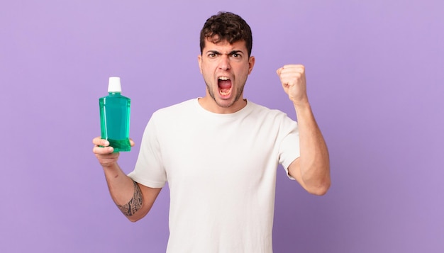 Homem com enxaguatório bucal gritando agressivamente com uma expressão de raiva ou com os punhos cerrados celebrando o sucesso