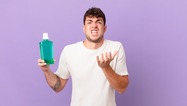 Homem com enxaguatório bucal parecendo desesperado e frustrado, estressado, infeliz e irritado, gritando e gritando