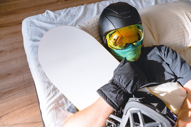 Homem com equipamento de esqui dormindo na cama com snowboard sonhando com montanhas