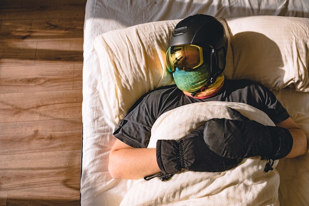 Homem com equipamento de esqui dormindo na cama sonhando com montanhas