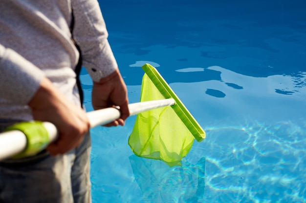 Homem com equipamento de skimmer net limpeza da piscina de lixo Serviço e manutenção da piscina Homem remove o lixo da água com uma seiva Serviço de limpeza de piscina Limpador de hotel