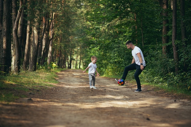 Homem com filho jogando futebol juntos, cavando bola na floresta, passam um tempo juntos se divertindo no fim de semana