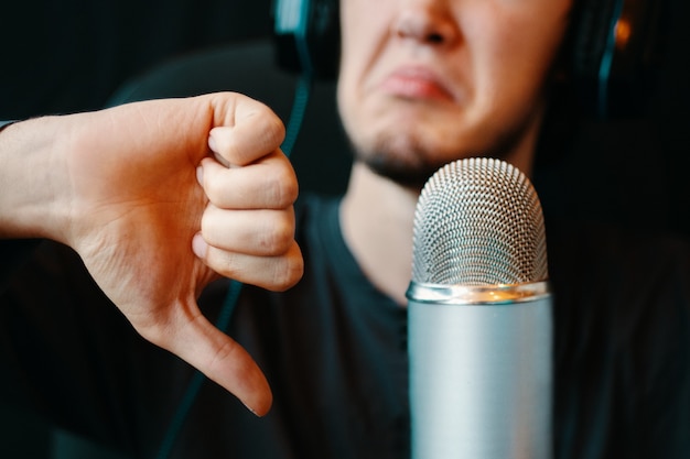 Homem com fones de ouvido e microfone no estúdio de podcast. gesto de antipatia. microfone vintage