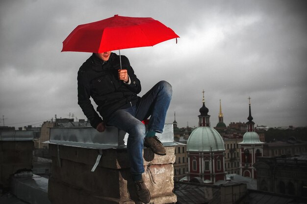 Homem com guarda-chuva vermelho sentado no telhado