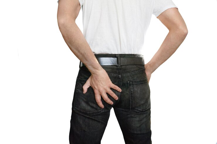 Foto homem com hemorróidas cara com dor em jeans preto segurando sua bunda com a mão esquerda em um fundo branco isolado
