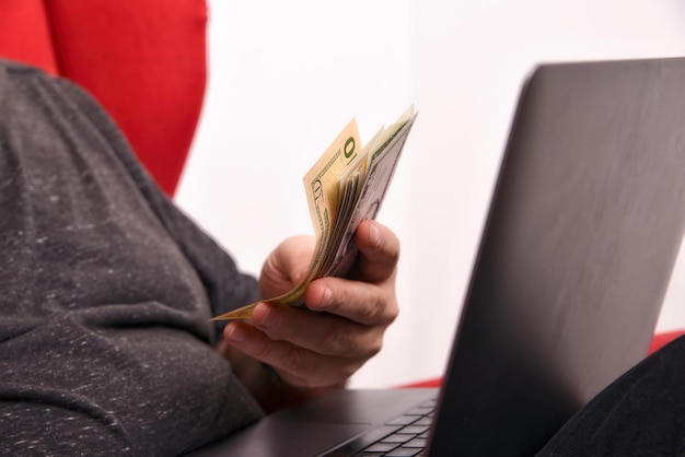 Homem com laptop no colo e dinheiro nas mãos closeup conceito de negócio online