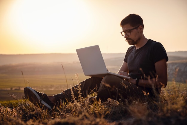 Homem com laptop sentado à beira de uma montanha com vistas deslumbrantes sobre o vale
