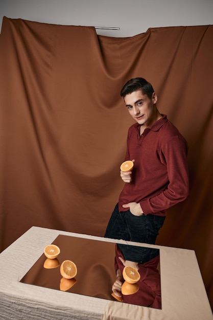 Homem com laranjas cortadas sobre a mesa e fundo de tecido refletido no espelho
