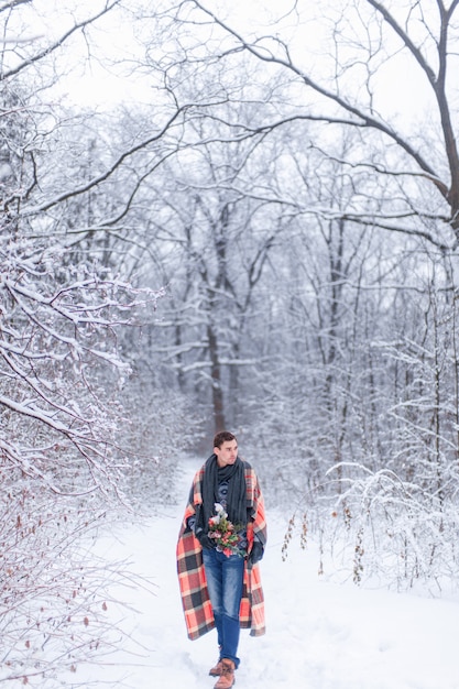 Homem com lenço coberto com manta em floresta de neve de inverno, retrato de corpo inteiro