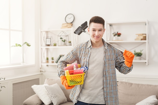 Homem com luvas de borracha segurando um frasco de spray de plástico, esponjas e pincéis na sala de estar, copie o espaço. Conceito de arrumação, serviços de limpeza e arrumação