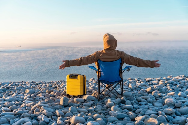 Homem com mala amarela relaxando sozinho em cadeiras de praia no conceito de estilo de vida de viagens à beira-mar