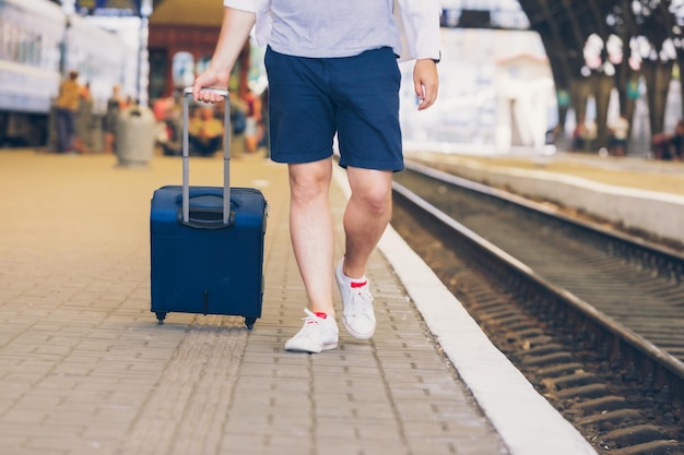 Homem com mala sobre rodas andando pela plataforma da estação ferroviária