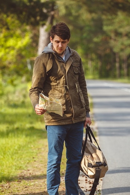 Homem com mapa e bolsa na mão caminhando em uma estrada