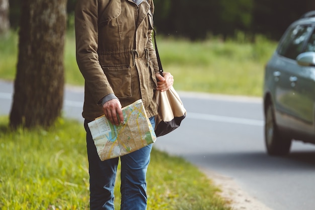 Homem com mapa e bolsa na mão caminhando em uma estrada