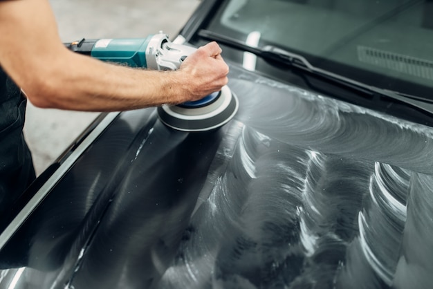 Homem com máquina de polir limpa capô do carro