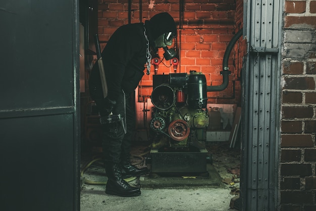 Homem com máscara de gás e um martelo na sala de máquinas.
