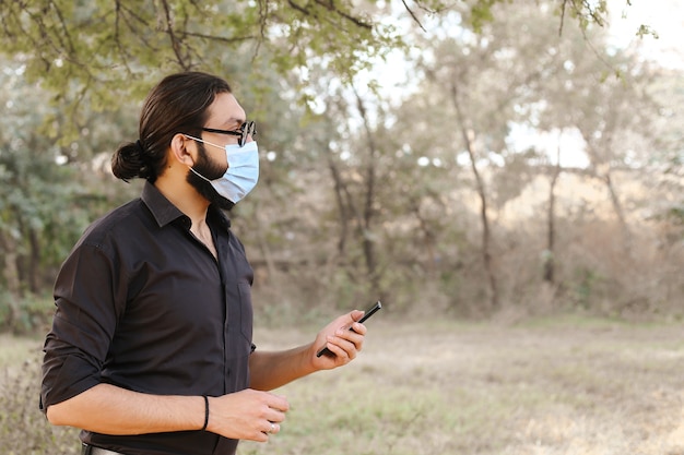 Homem com máscara de proteção usando um celular na natureza