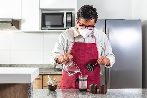 Homem com máscara derramando água quente em uma prensa francesa para preparar café em uma cozinha doméstica ou restaurante