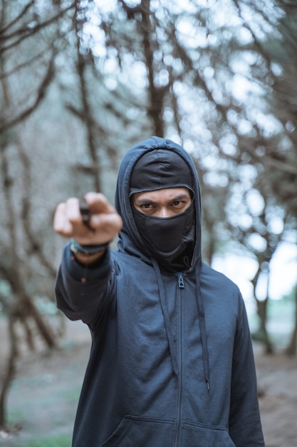 Homem com máscara e faca e roupas pretas em uma floresta