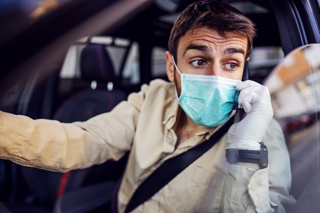 Homem com máscara e luvas dirigindo um carro, falando no smartphone do telefone móvel. Prevenção de infecções e controle de epidemia. Pandemia mundial. Fique seguro.