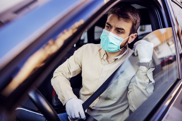 Homem com máscara e luvas, dirigindo um carro. Prevenção de infecções e controle de epidemia. Pandemia mundial. Fique seguro.