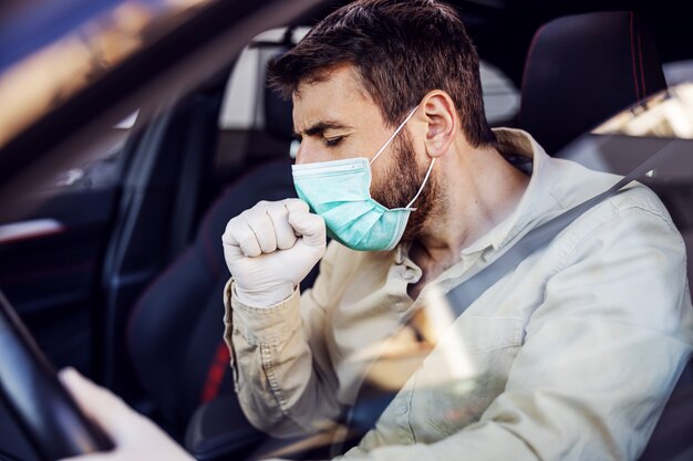 Homem com máscara e luvas dirigindo um carro tossindo. Prevenção de infecções e controle de epidemia. Pandemia mundial. Fique seguro.
