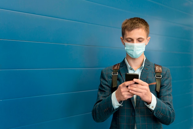 Homem com máscara médica e mochila usando smartphone