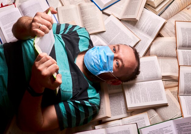 Homem com máscara médica e muitos livros de papel