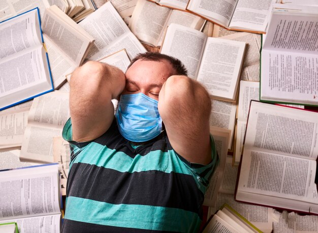 Homem com máscara médica e muitos livros de papel