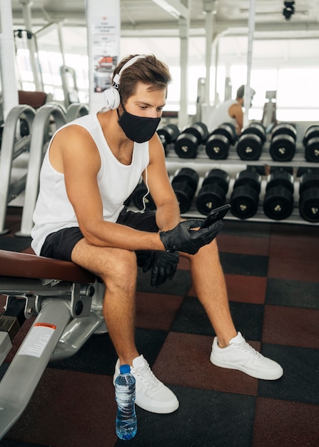 Homem com máscara médica ouvindo música no fone de ouvido enquanto usa o smartphone