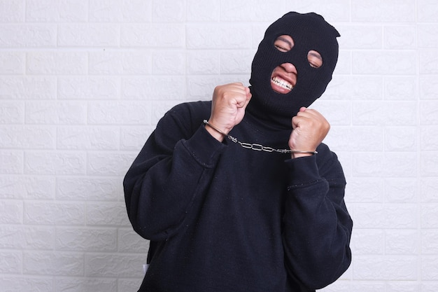 Homem com máscara preta e roupa suspeita de assalto usando algemas