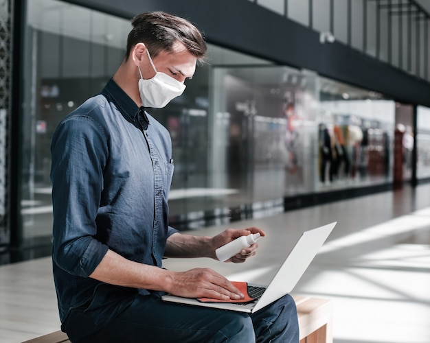 Homem com máscara protetora desinfeta seu laptop. pandemia na cidade