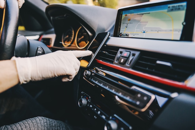 Homem com máscara protetora e luvas dirigindo um carro, digitando no smartphone do celular. epidemia. fique seguro.