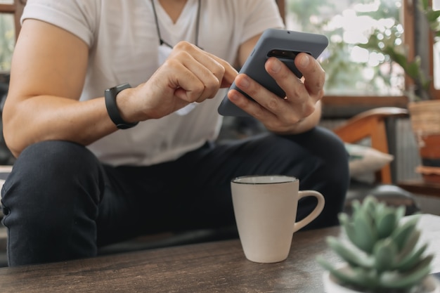 Homem com máscara usando smartphone e tomando café no café