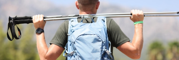 Homem com mochila olhando montanhas e segurando bengalas na vista traseira das mãos