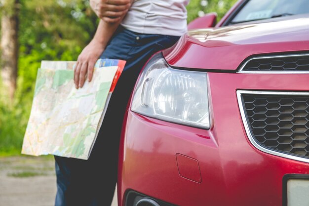 Homem com o mapa em mãos ao lado de um carro na floresta