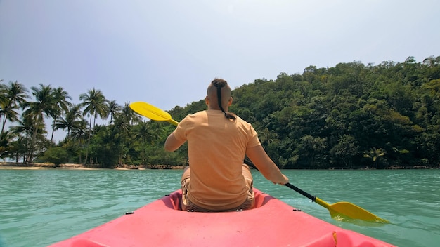 Homem com óculos de sol e chapéu enfileira canoa de plástico rosa ao longo do mar ag