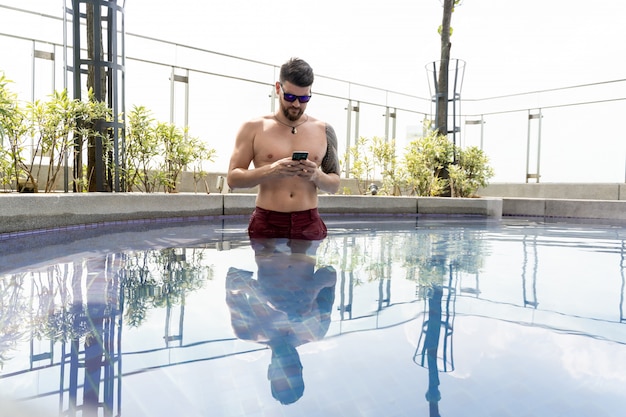 Homem com óculos de sol usando seu celular em uma piscina