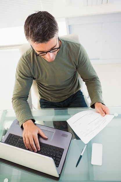 Foto homem com óculos que lêem papel e usando laptop