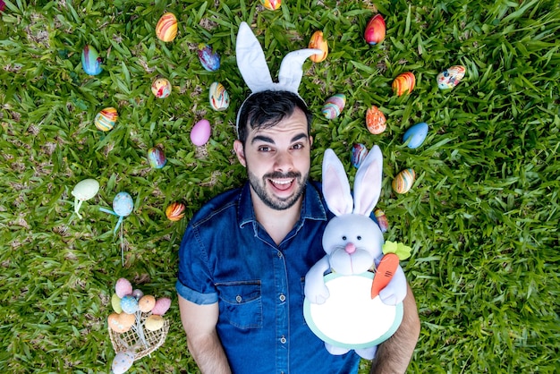 Homem com orelhas de coelho da páscoa deitado na grama ovos de páscoa coloridos